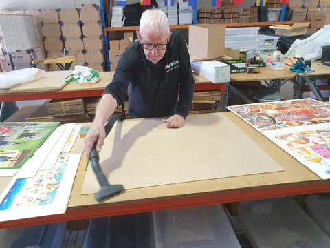 A photo of a man vacuuming the dust off of a base for a new puzzle