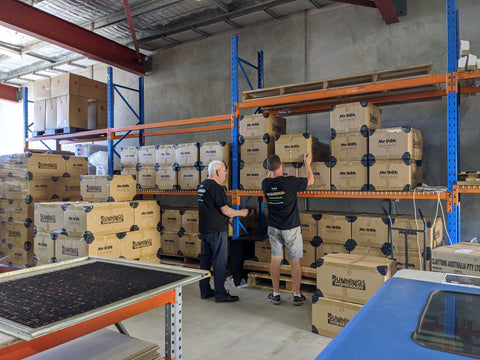 A photo of two men stacking cardboard boxes in a warehouse - the boxes are labelled with either Mr Bob Puzzles logos or Bunnings Warehouse logos