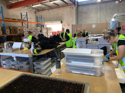 An internal photo of the Mr Bob Puzzles factory with various boxes stacked around the place and various workers with hi-vis clothes working.
